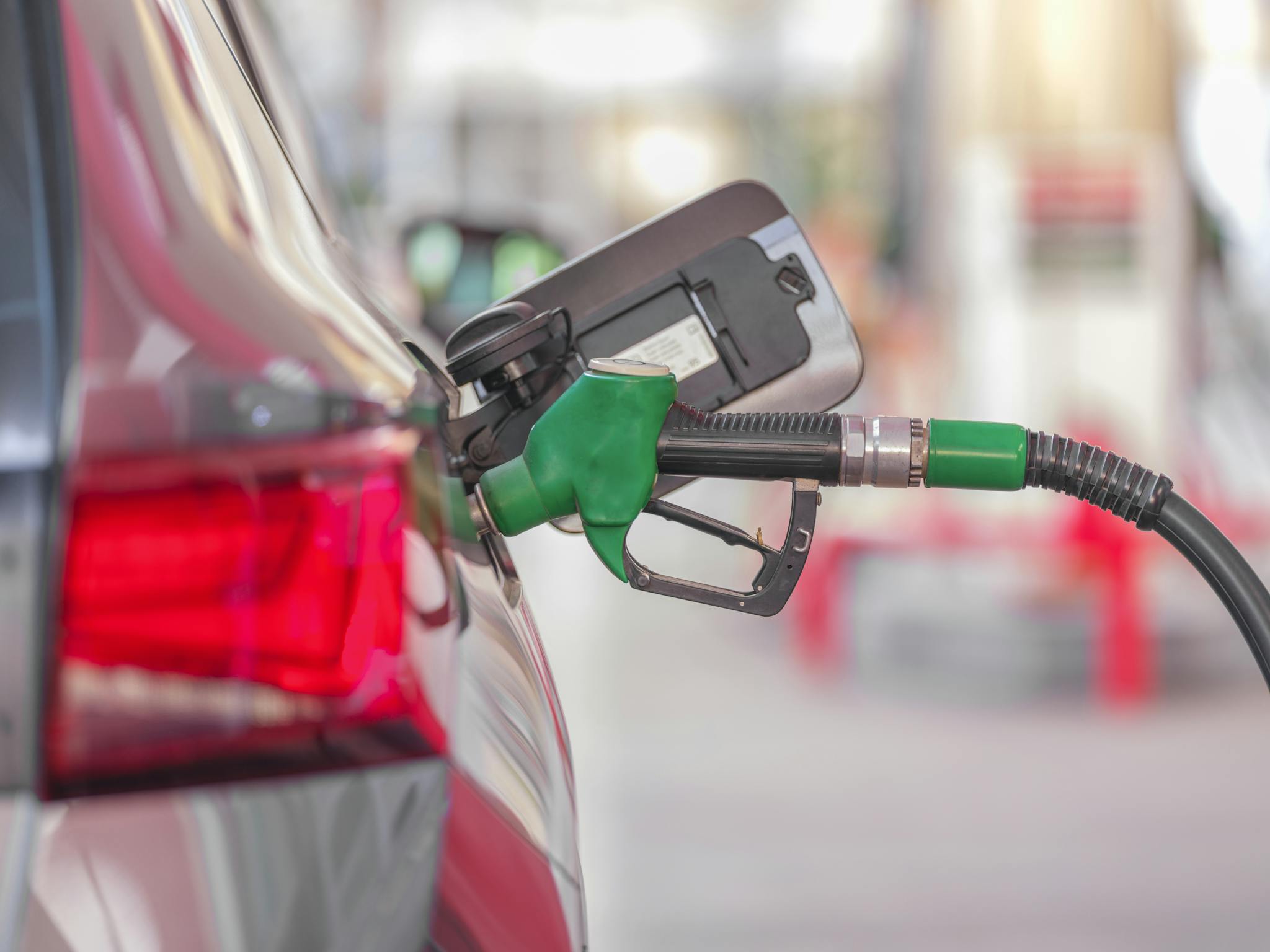 A close-up view of a fuel pump nozzle inserted into a car's tank at a gas station.