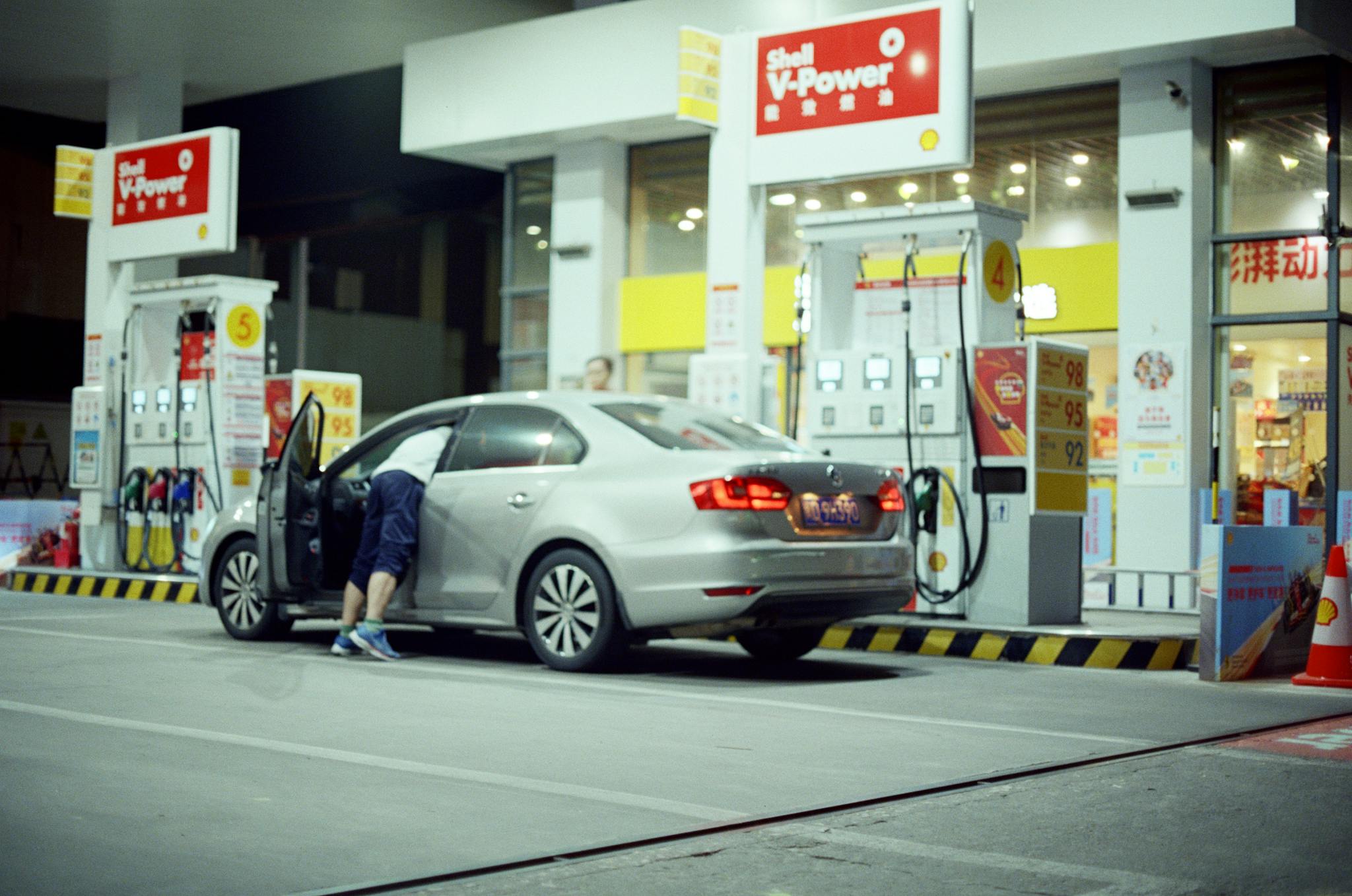 A person refuels their car at an illuminated Shell gas station at night.