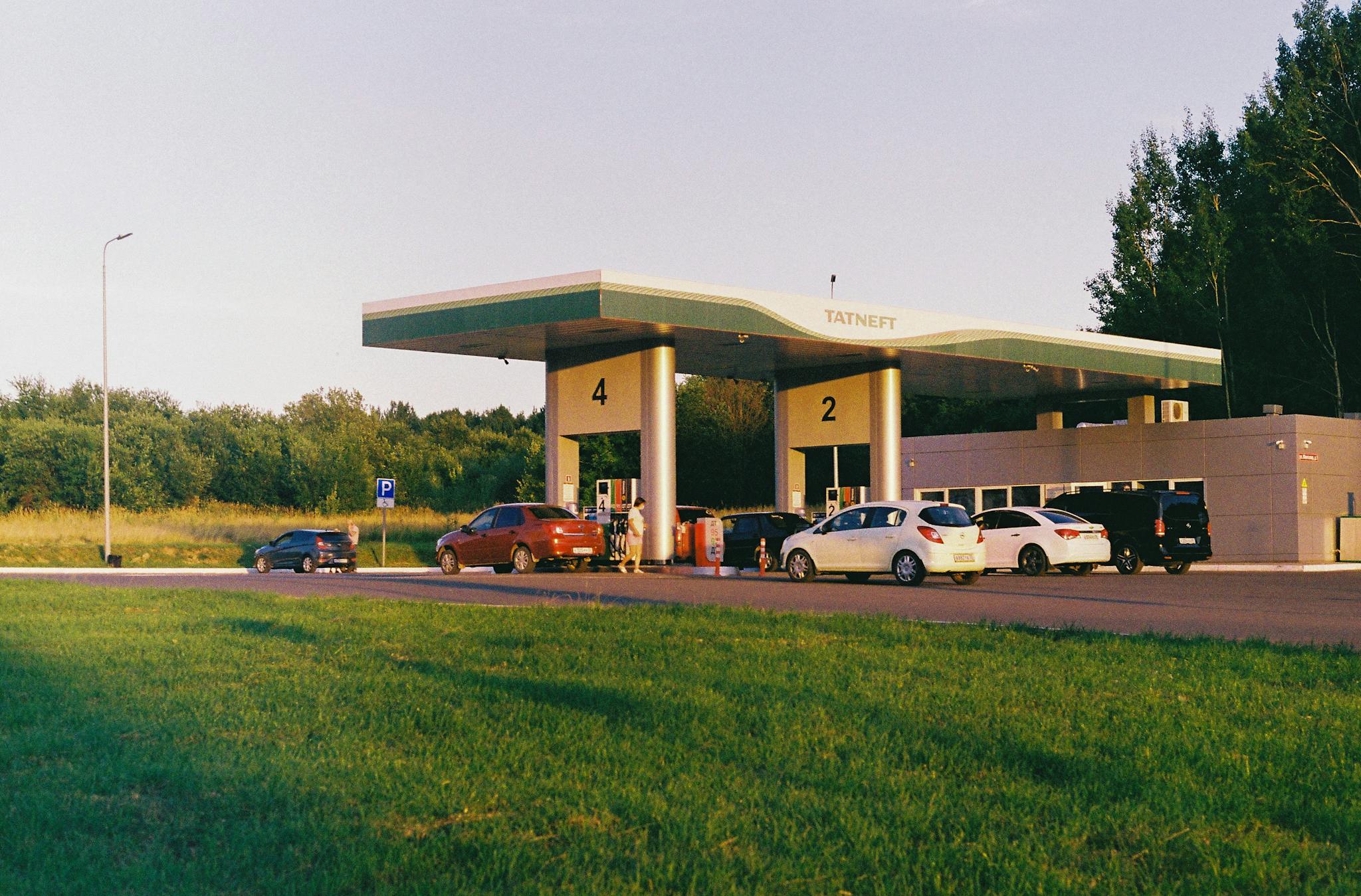 Cars lined up at a Tatneft gas station with a green landscape backdrop during the day.