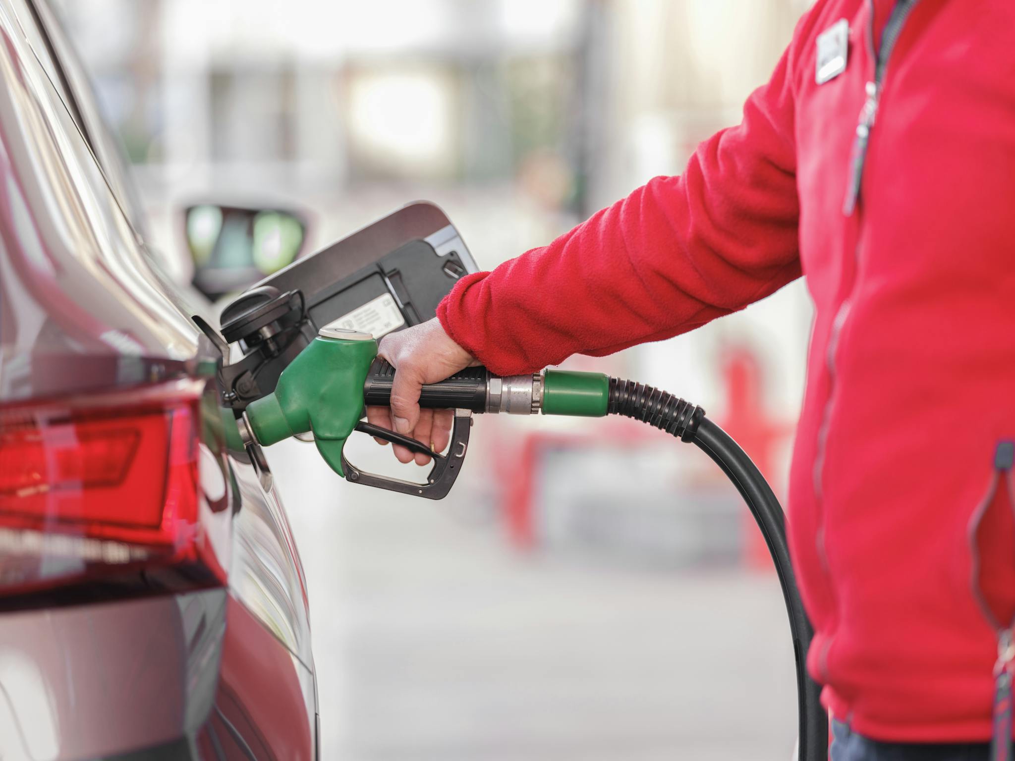Close-up of a person refueling a car with a green hose at a gas station.