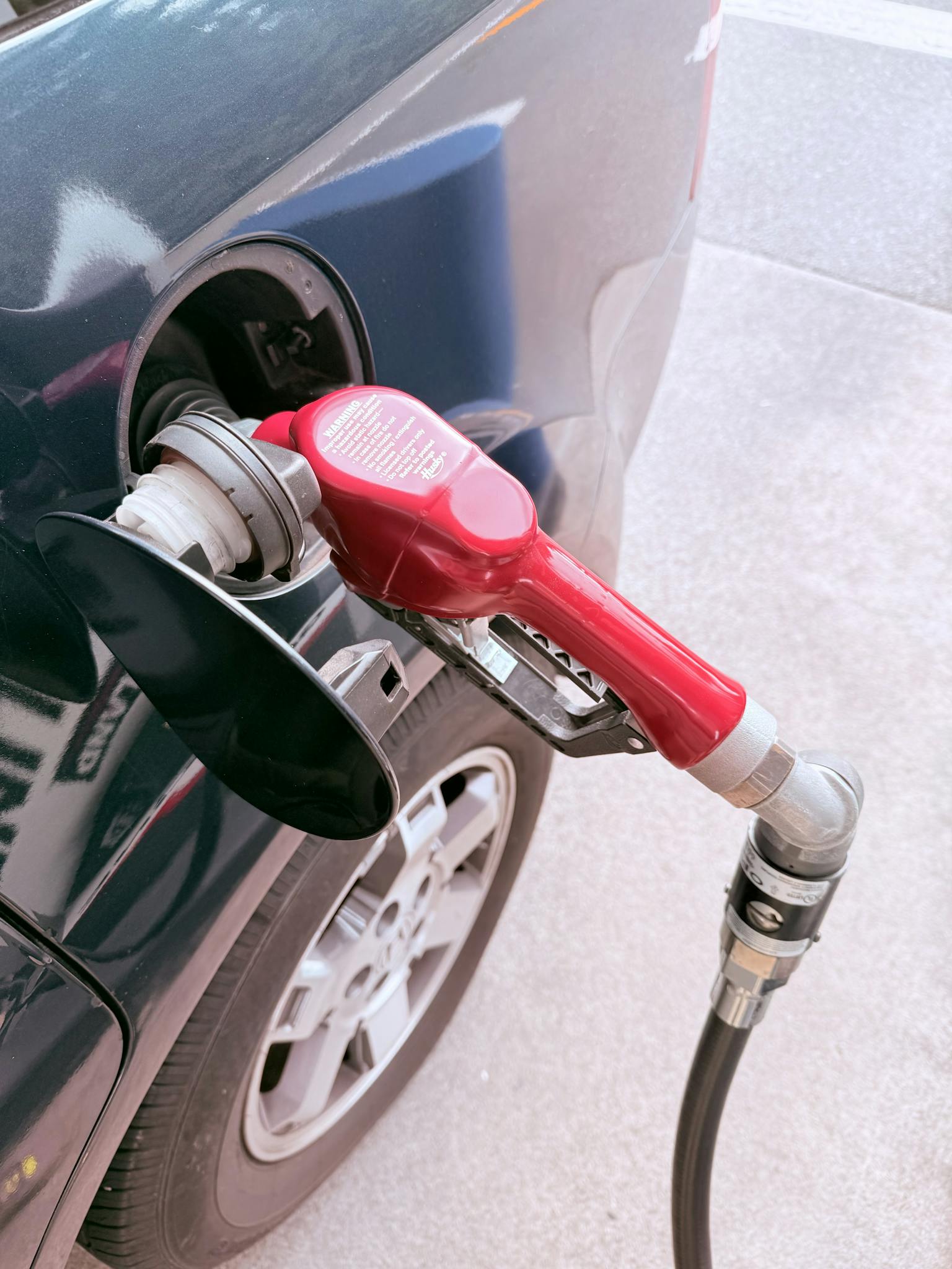 Close-up of a red gas pump fueling a car at a gas station, depicting the refueling process.
